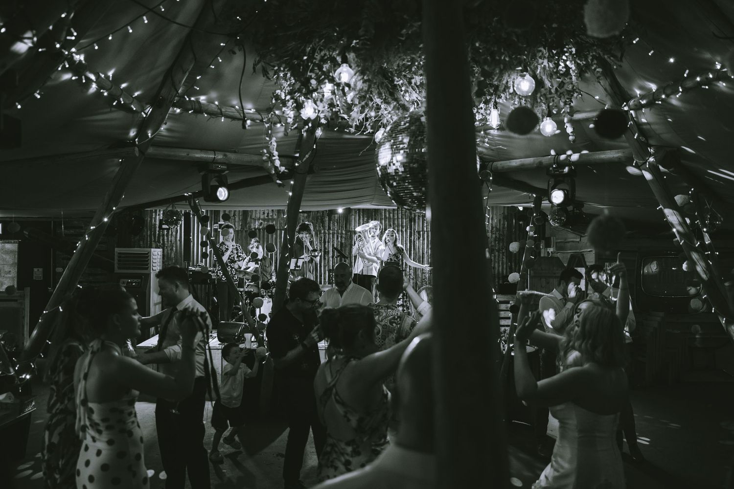 Black and white photo of guests dancing under fairy lights at an outdoor evening wedding reception Tipi Wedding at Kendal Brewery