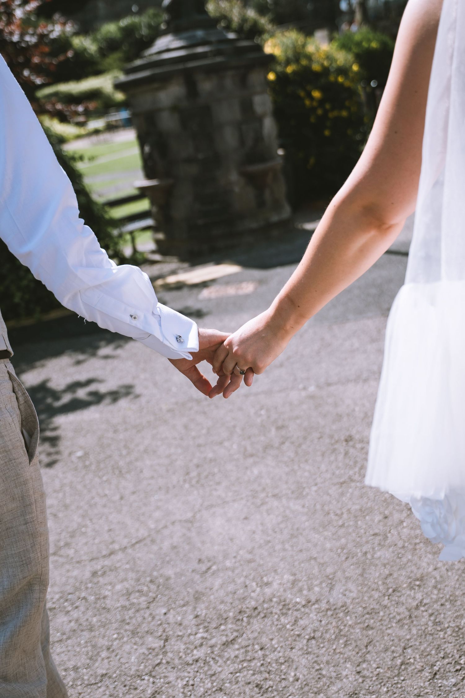Close-up of bride and groom holding hands outdoors, bride wearing veil, groom in white dress shirt in Kendal