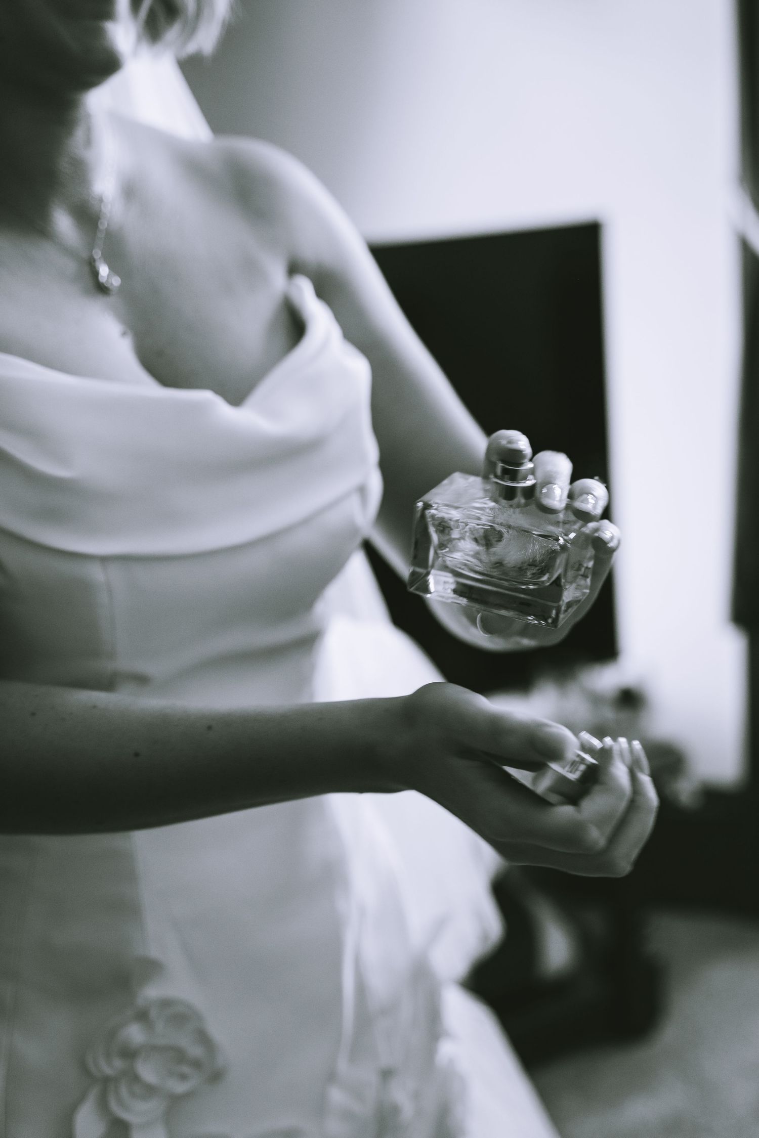 Black and white photo of a bride in a white dress applying perfume on her wrist before her wedding in The Lake District