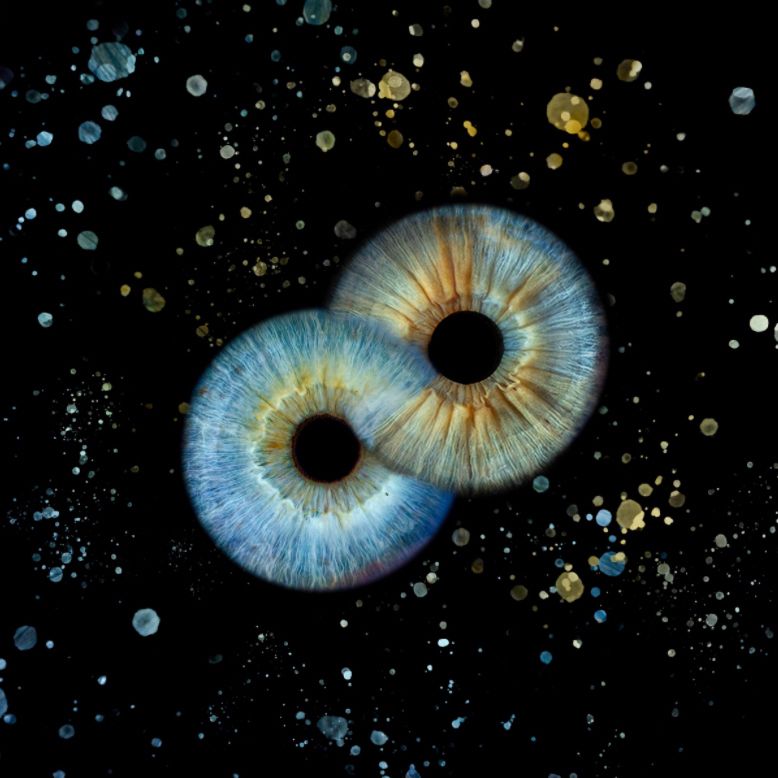 Two blue human irises forming infinity symbol surrounded by golden bokeh on black background.