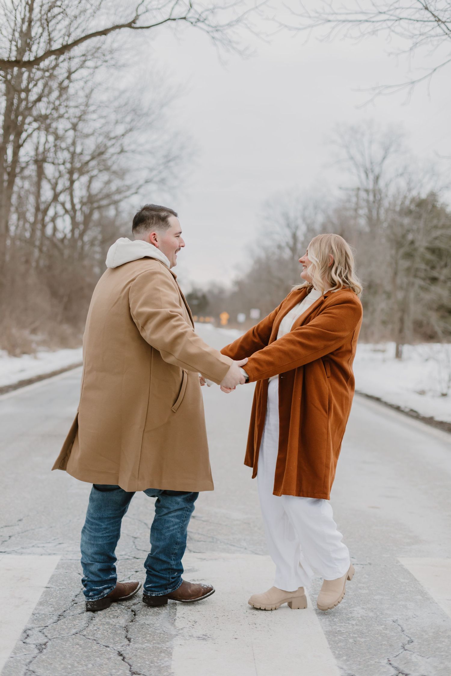 Two people in winter attire playfully interact on a snowy path surrounded by bare trees.