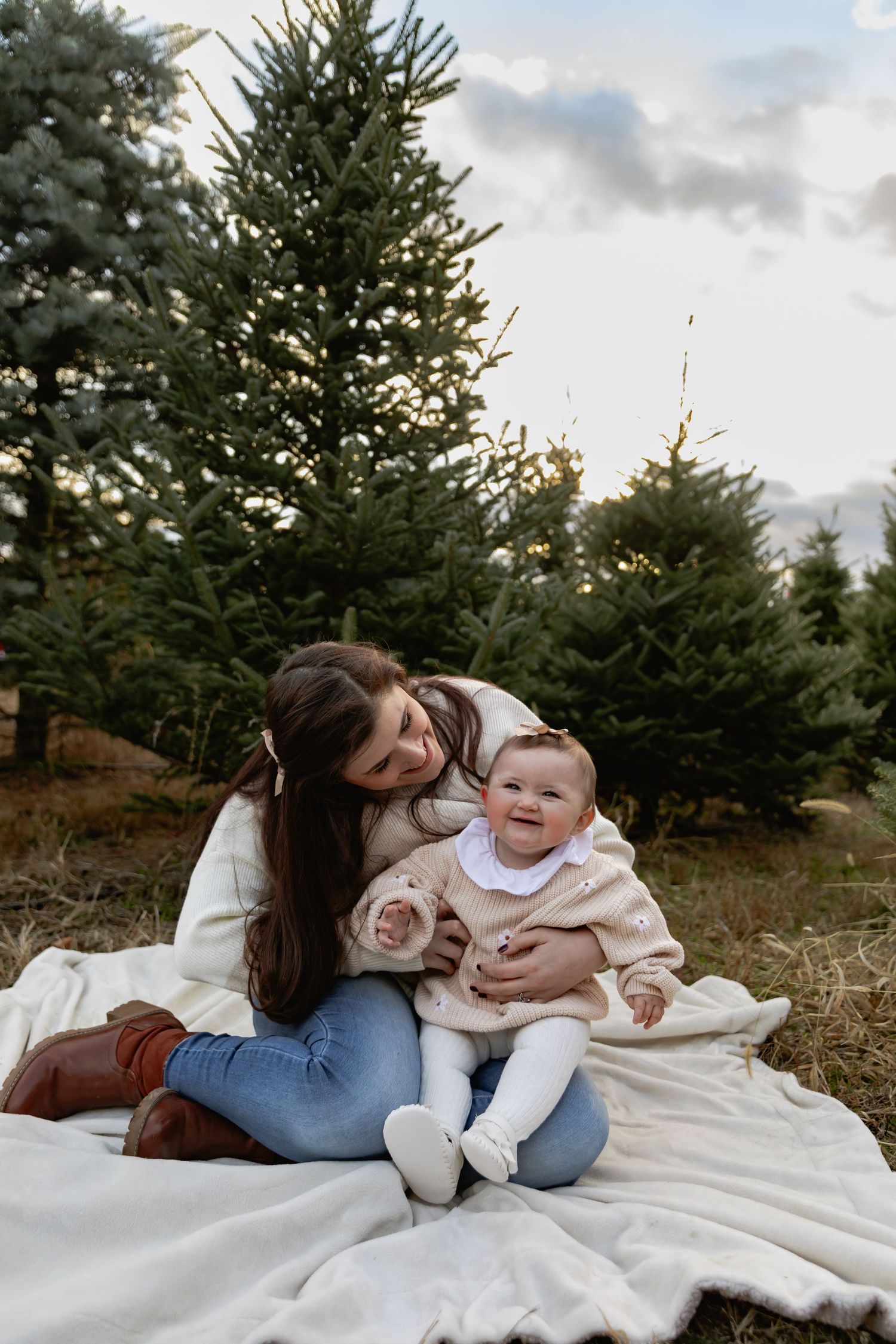 A heartwarming outdoor family moment on a white blanket surrounded by evergreen trees during golden hour.