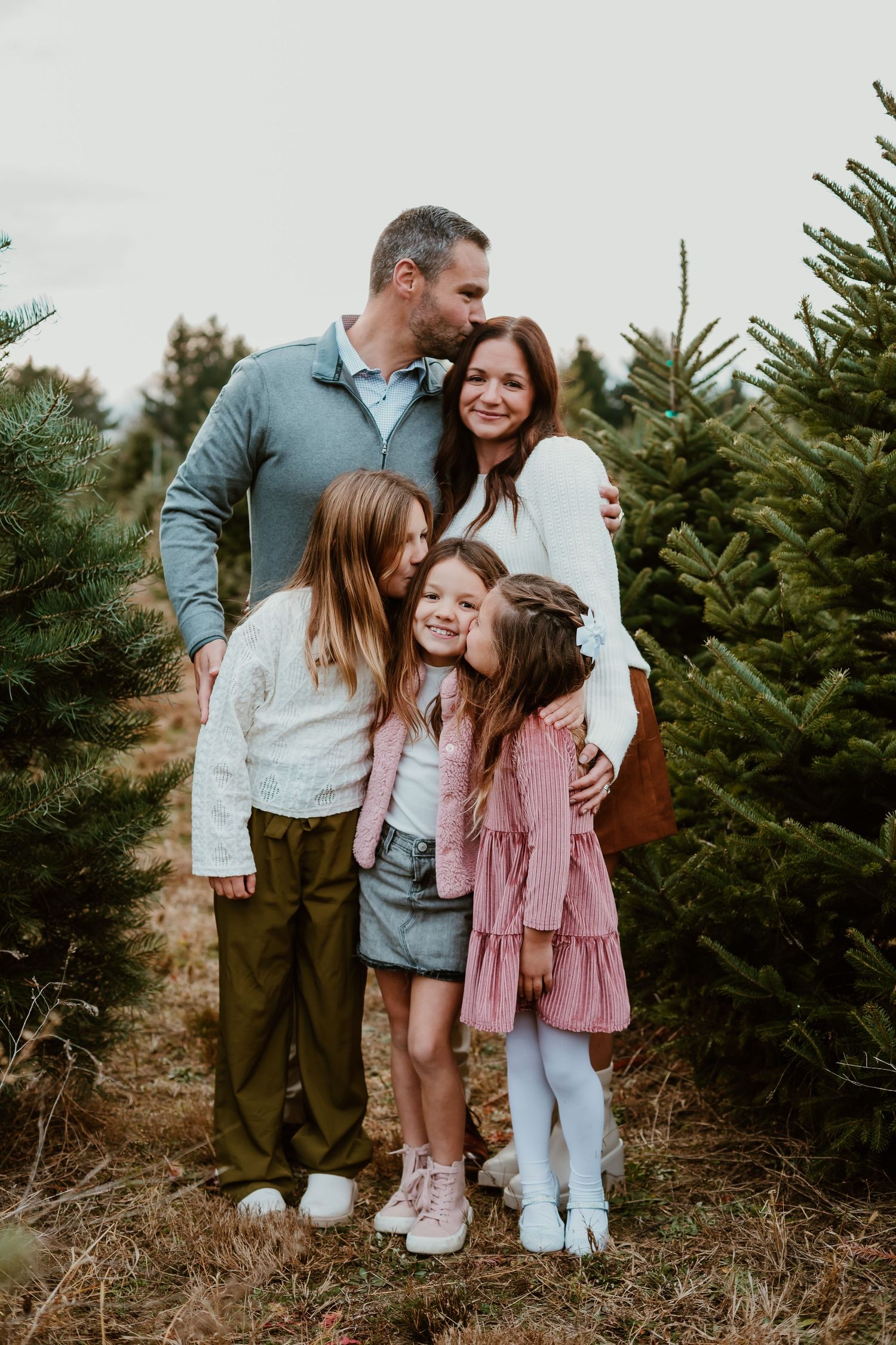 A family poses together among evergreen trees at a Christmas tree farm.