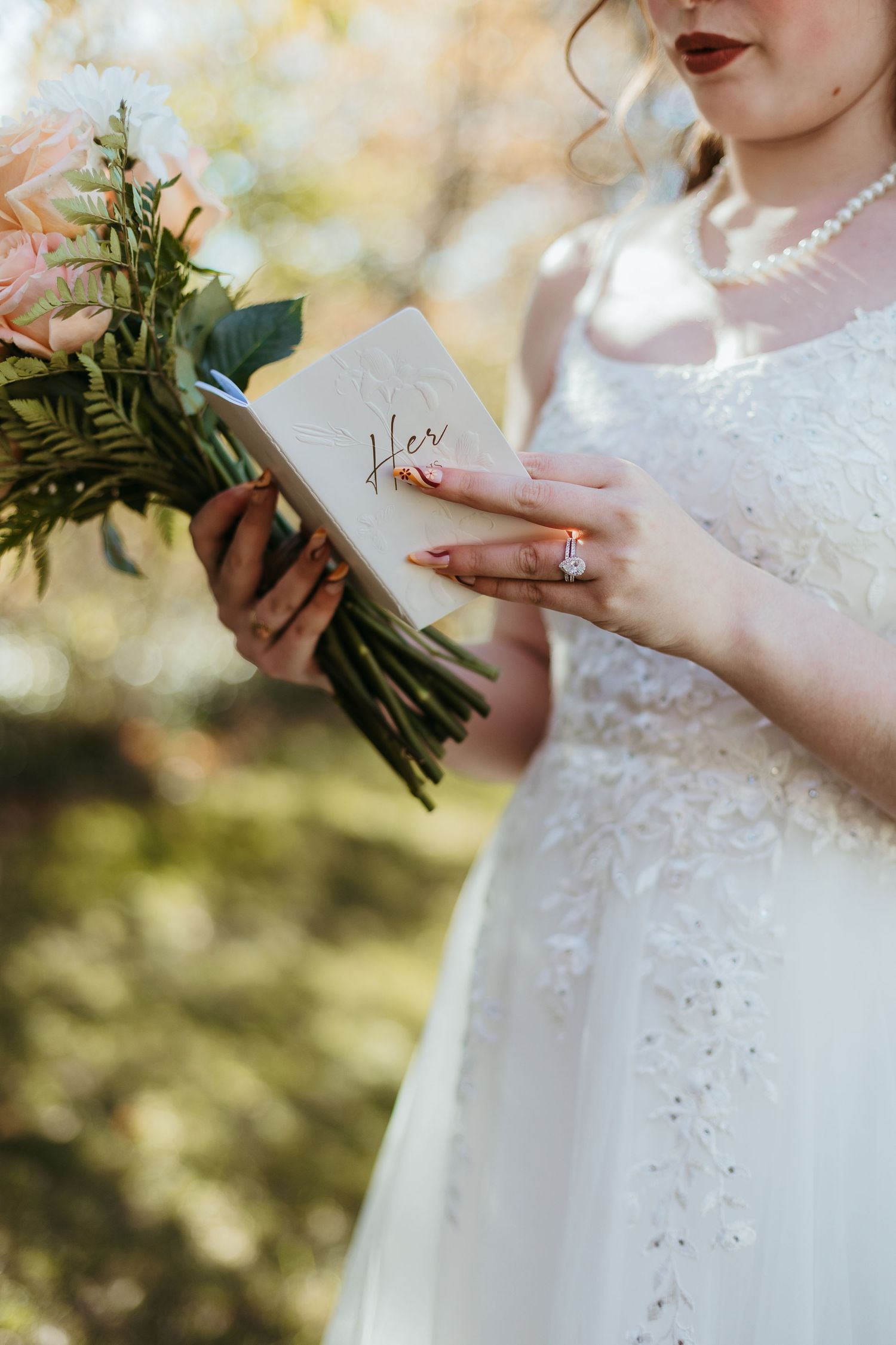 Bride holding wedding bouquet and vows book in white lace dress.