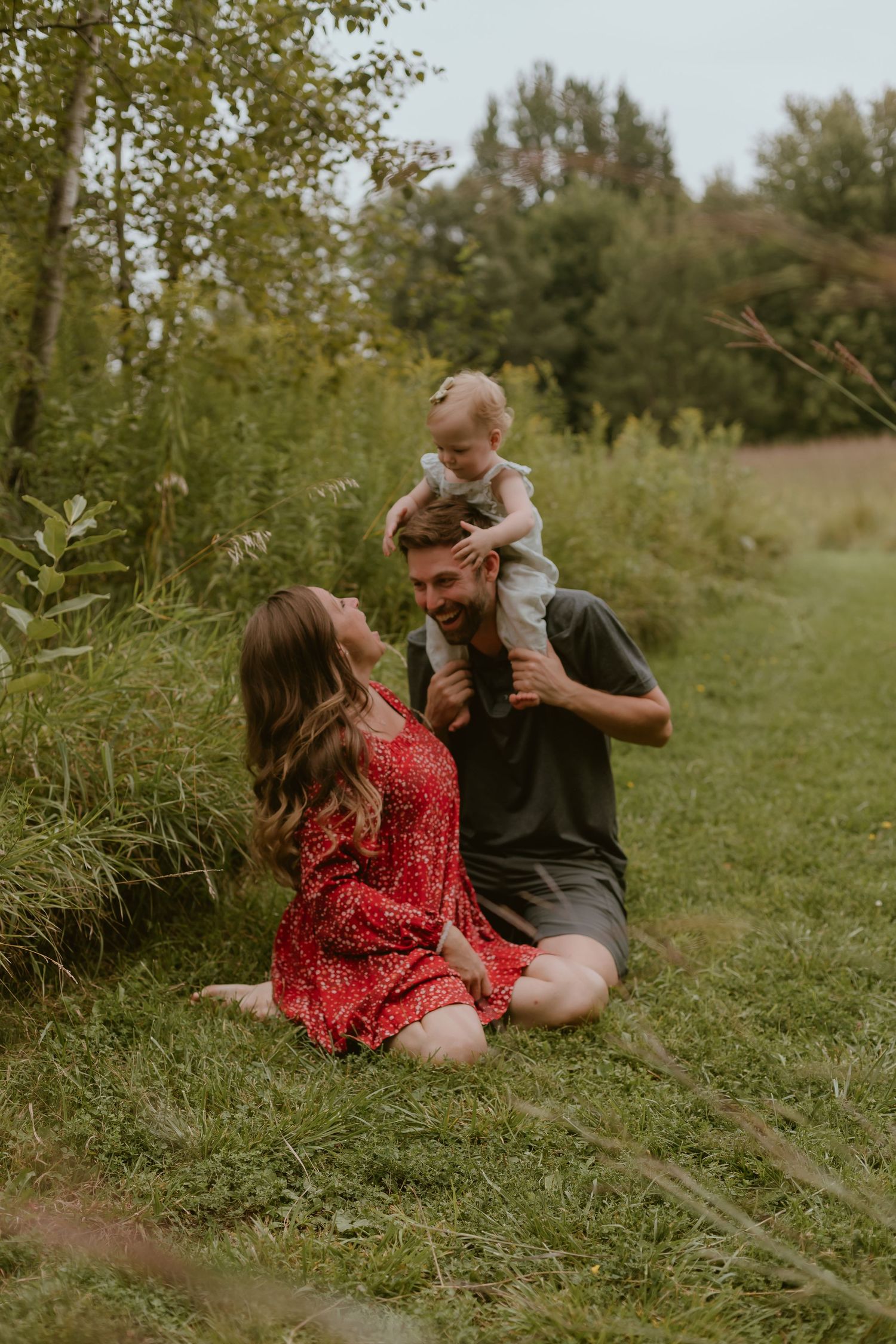 A family shares a joyful moment together sitting in tall grass on a sunny summer day.