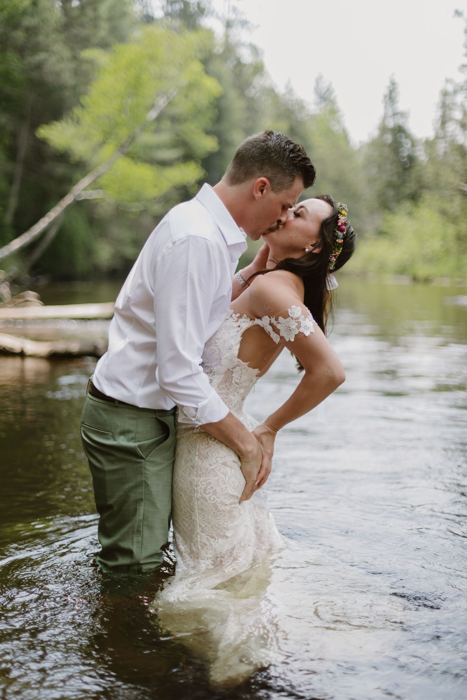 Romantic wedding couple stands in river water creating intimate moments in a series of artistic shots near forest trees.