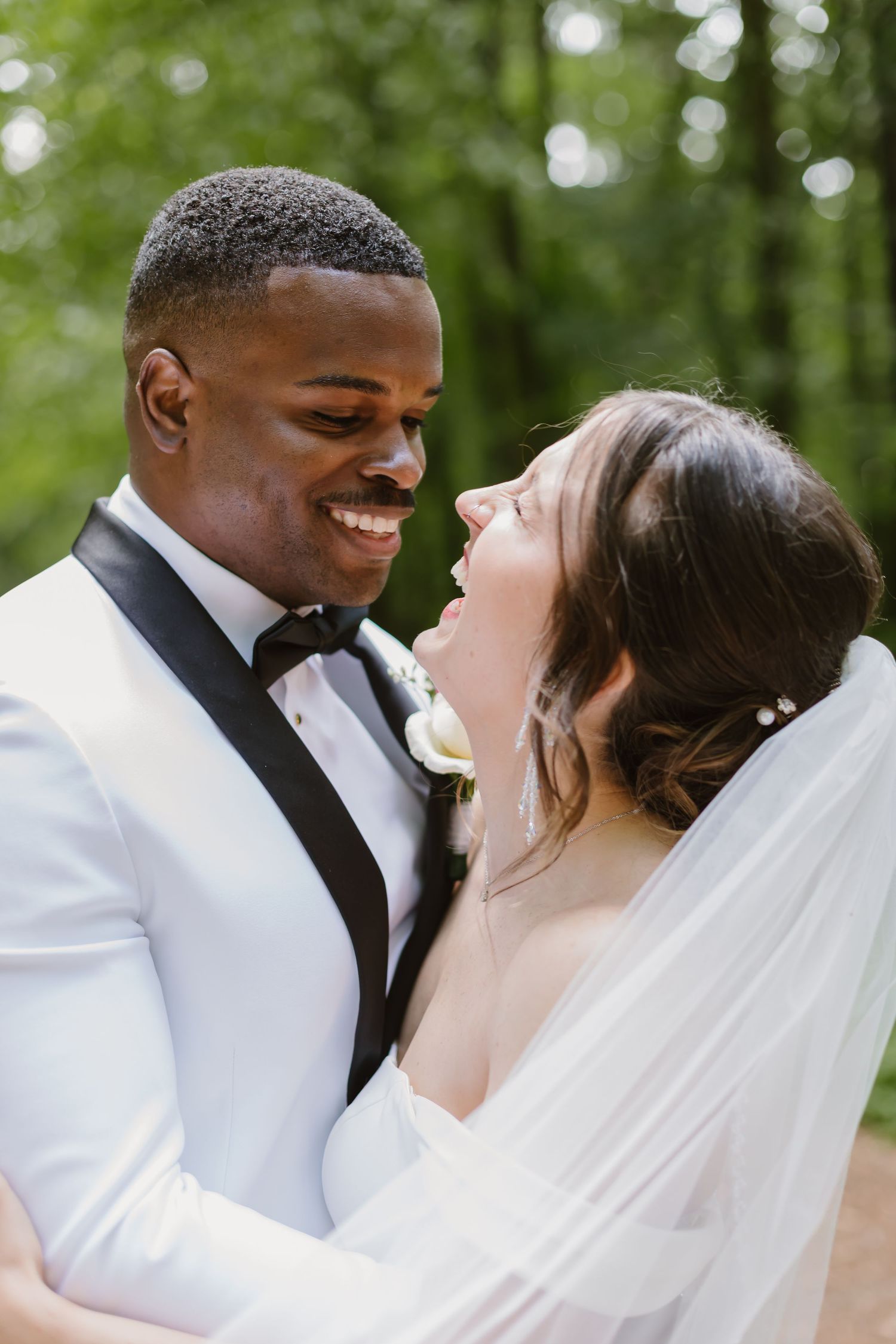 A bride and groom share intimate moments during their outdoor wedding photoshoot in a lush green forest setting.