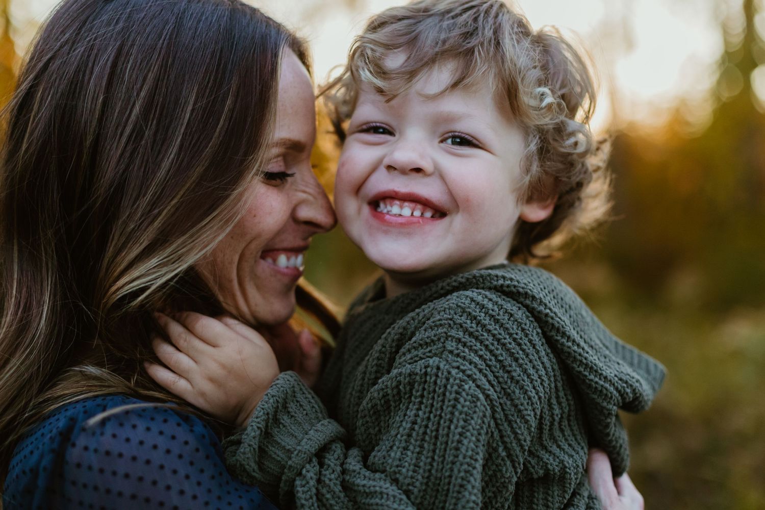 A parent and child share a joyful intimate moment outdoors during golden hour.