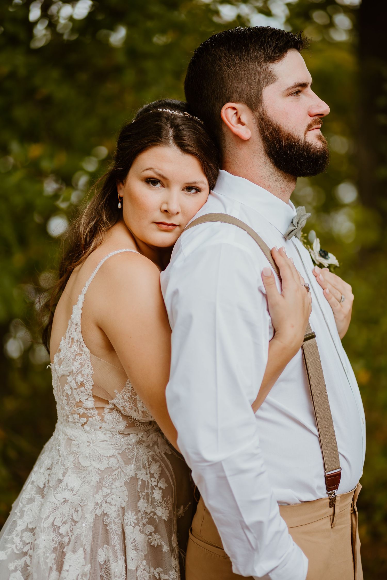 A romantic wedding photo showcasing the bride in a lace dress embracing the groom in casual attire outdoors.