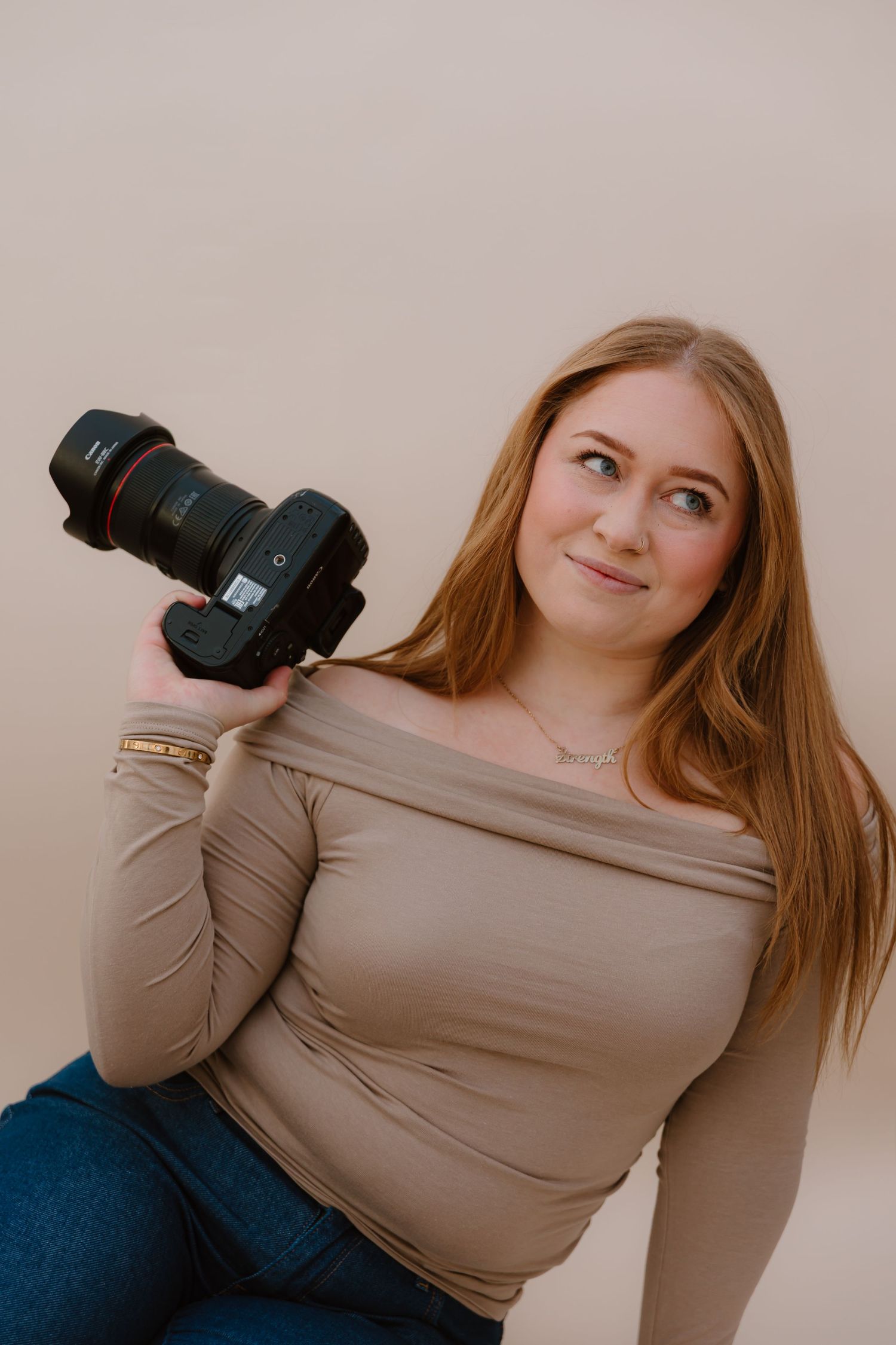 Creative portrait with professional camera and casual attire against neutral background.