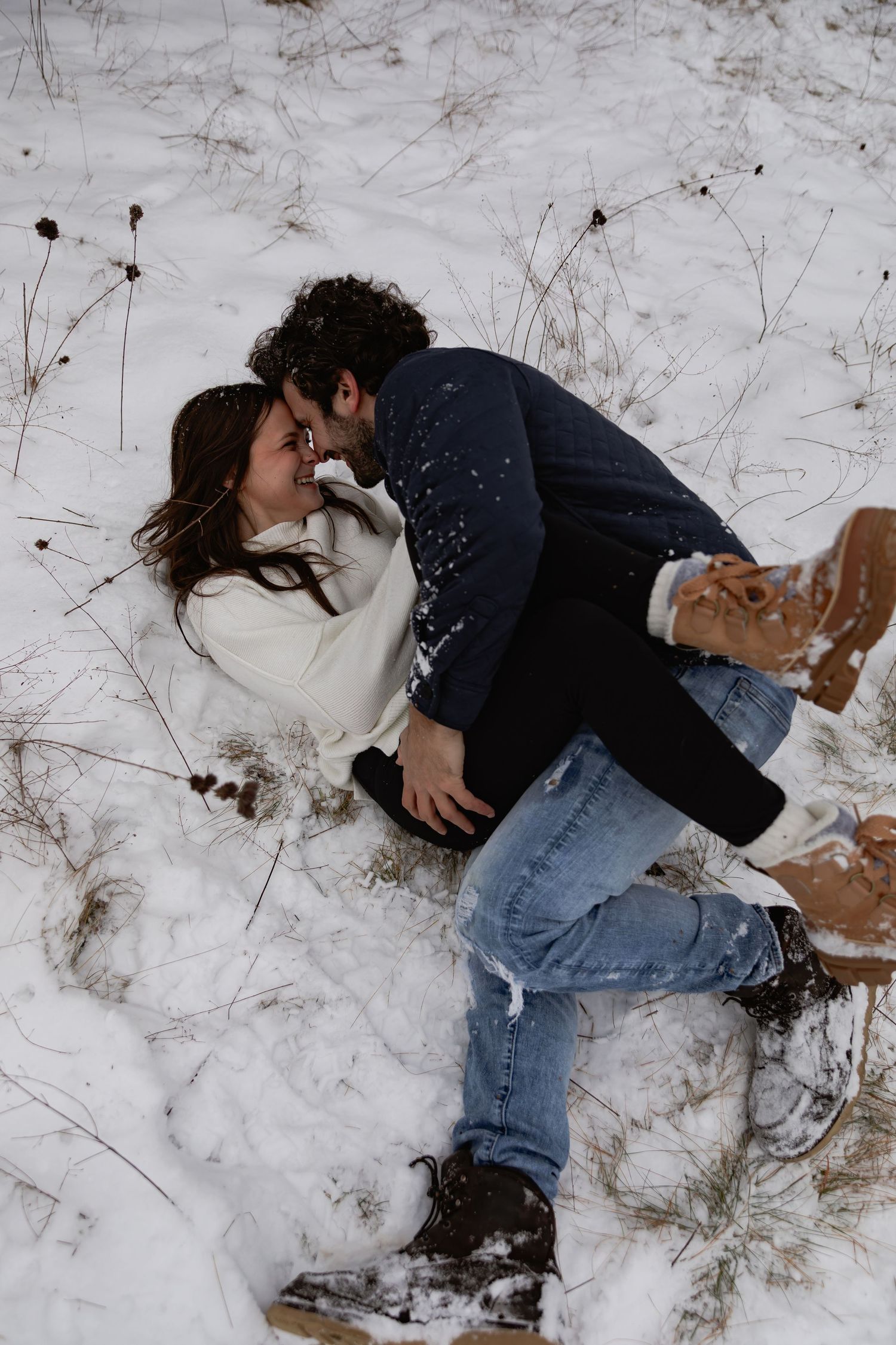 A person lying in the snow wearing jeans and a dark jacket while making snow angels.