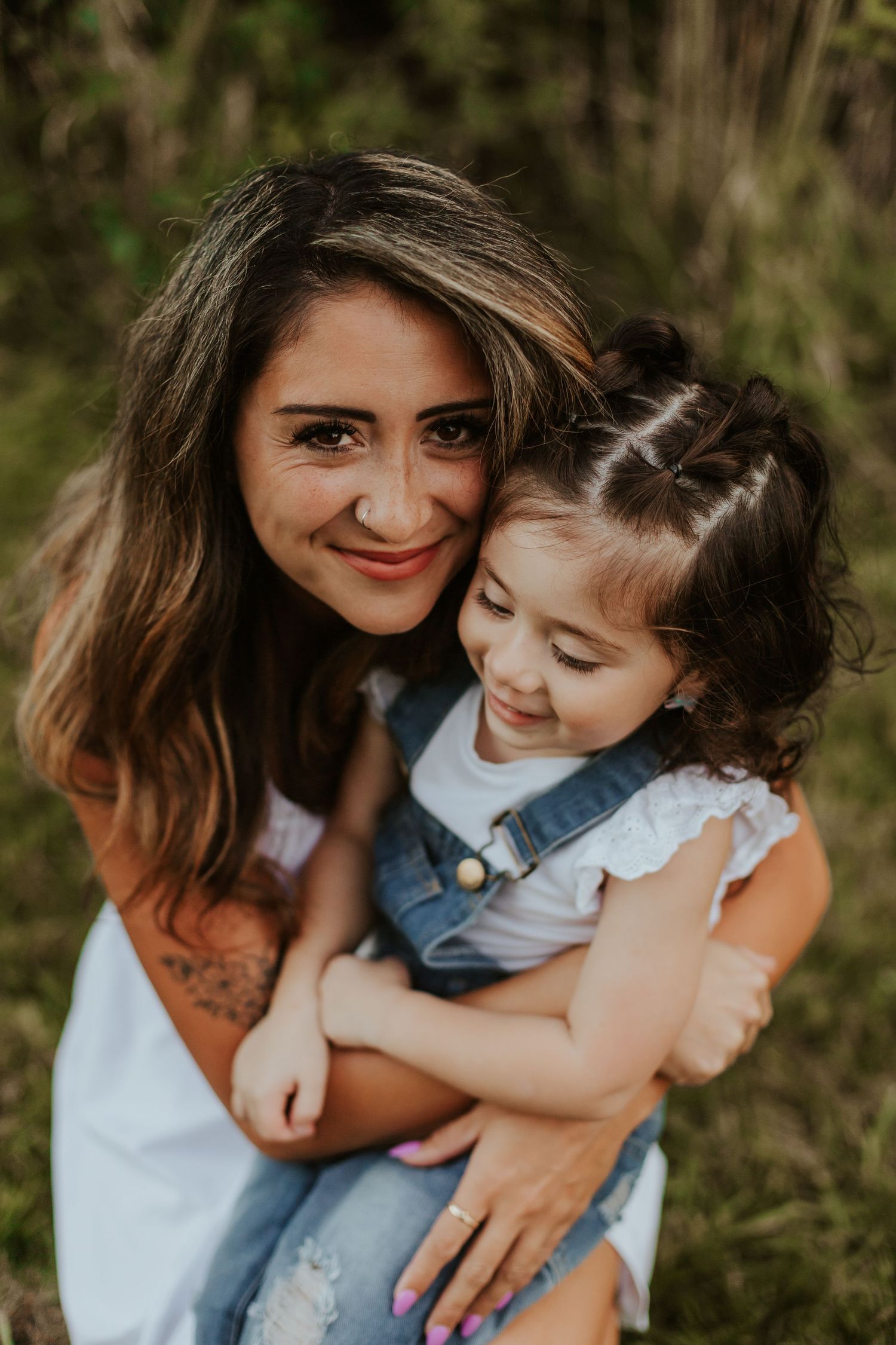 A mother and daughter share a tender moment outdoors, embracing and smiling together in natural lighting.