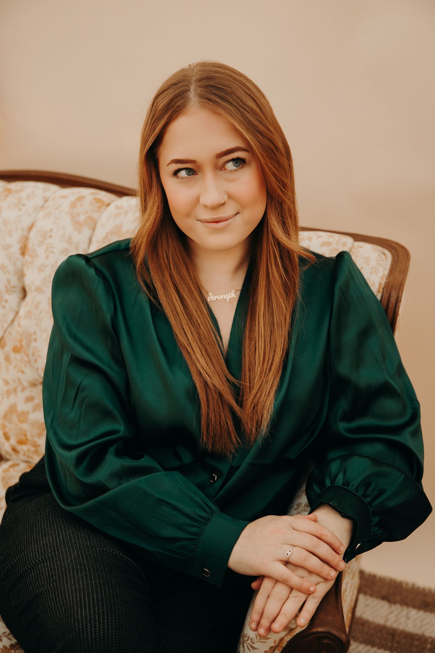 Portrait of a professional wearing an emerald green silk blouse while sitting on a floral patterned chair.