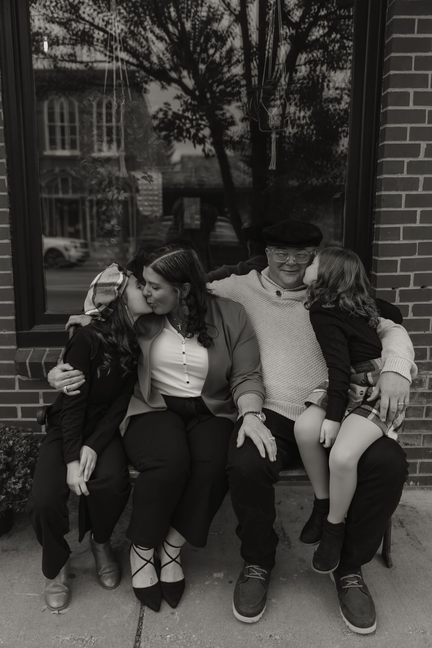 A black and white collage of four similar photos showing people sitting against a brick wall.