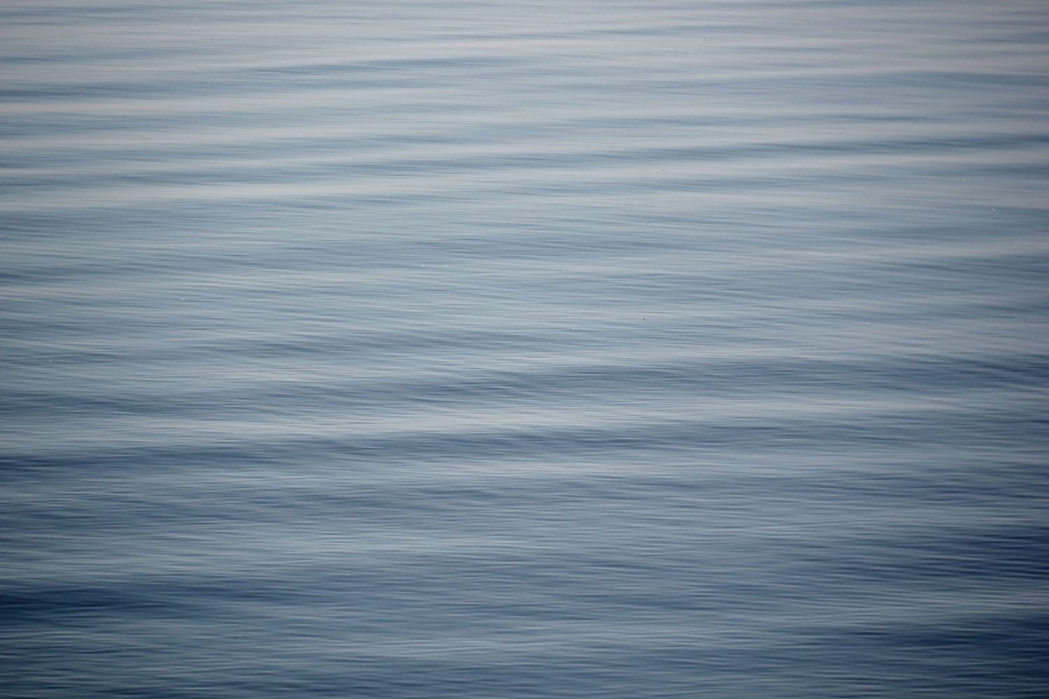 Slow shutter speed capture of ripples on a lake showing blurred horizontal lines of white and dark and light blue.