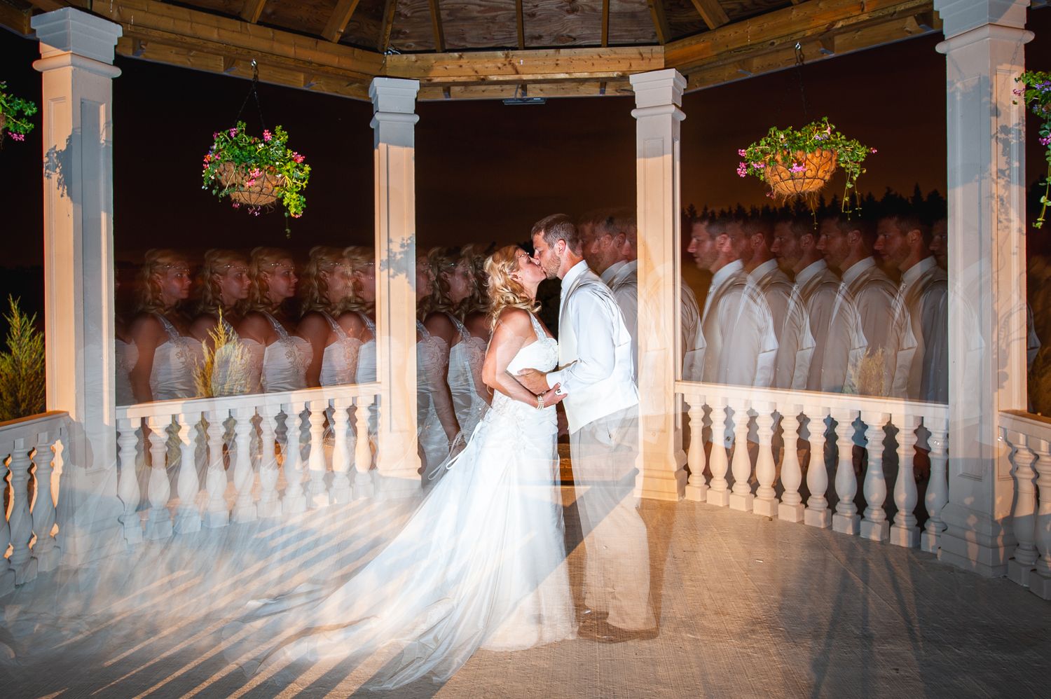 Newlyweds share tender moment in an elegant gazebo with white columns decorated with hanging plants.