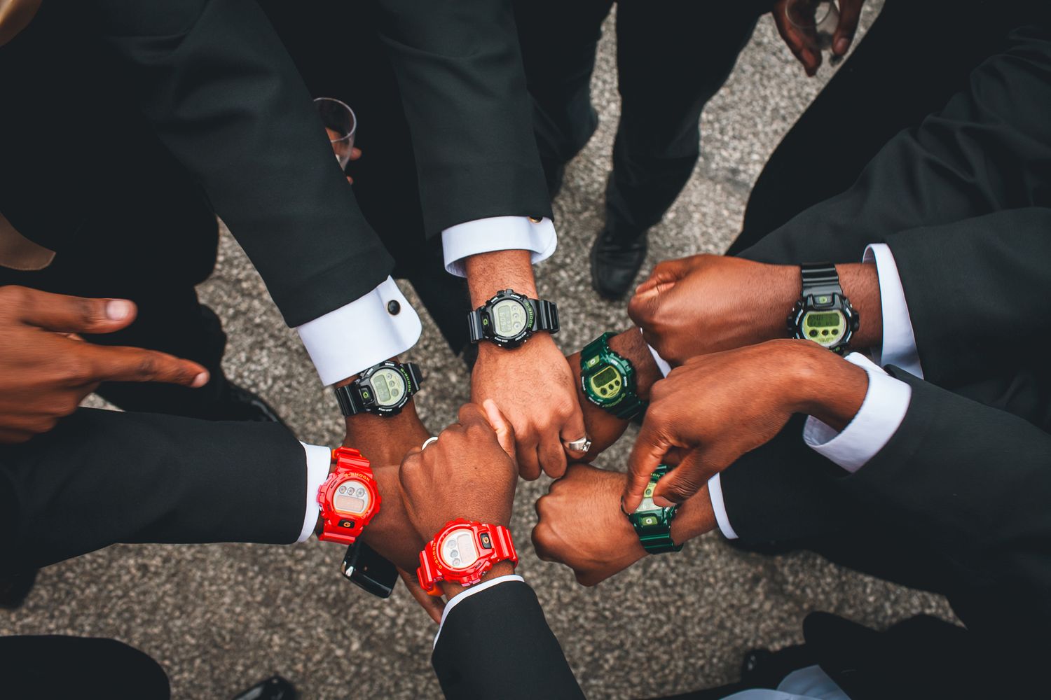 A group of men in formal suits showing off their matching luxury watches in a circle formation.
