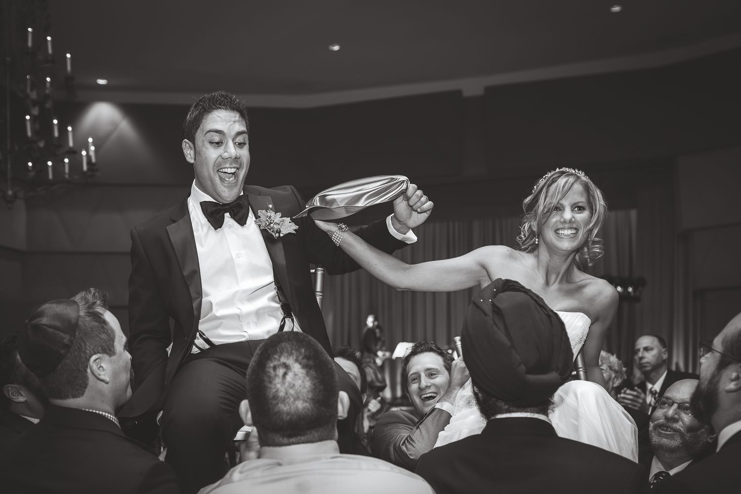 Black and white photo of people dancing and celebrating at a lively wedding reception on a dance floor.