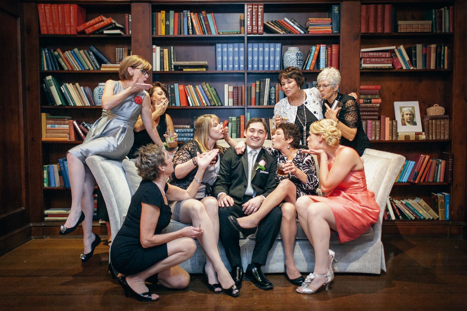 A group gathers on a couch in front of a floor-to-ceiling library bookshelf in vintage 1950s style clothing.