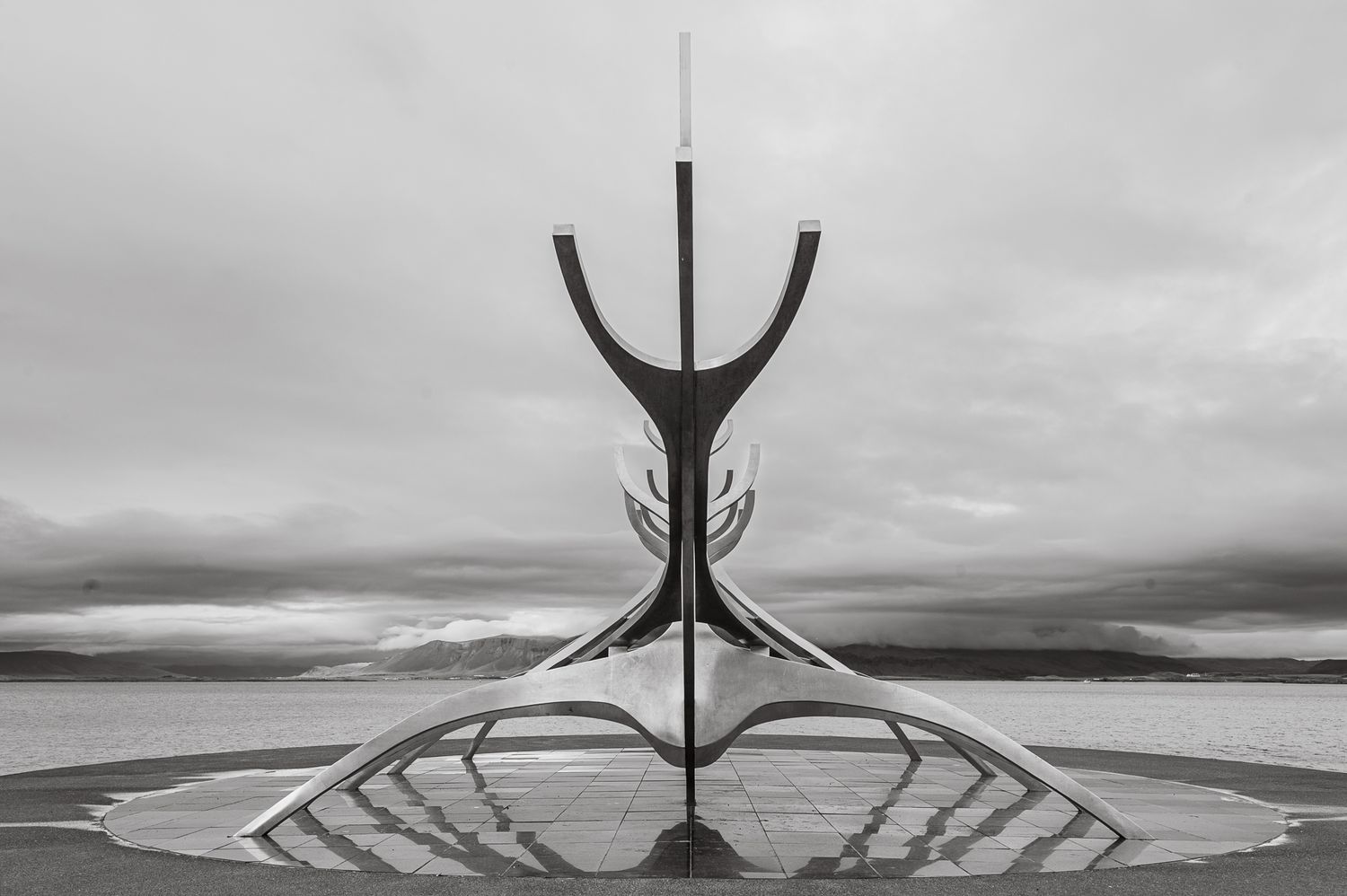 Abstract black and white architectural sculpture against moody sky with mountains in background.