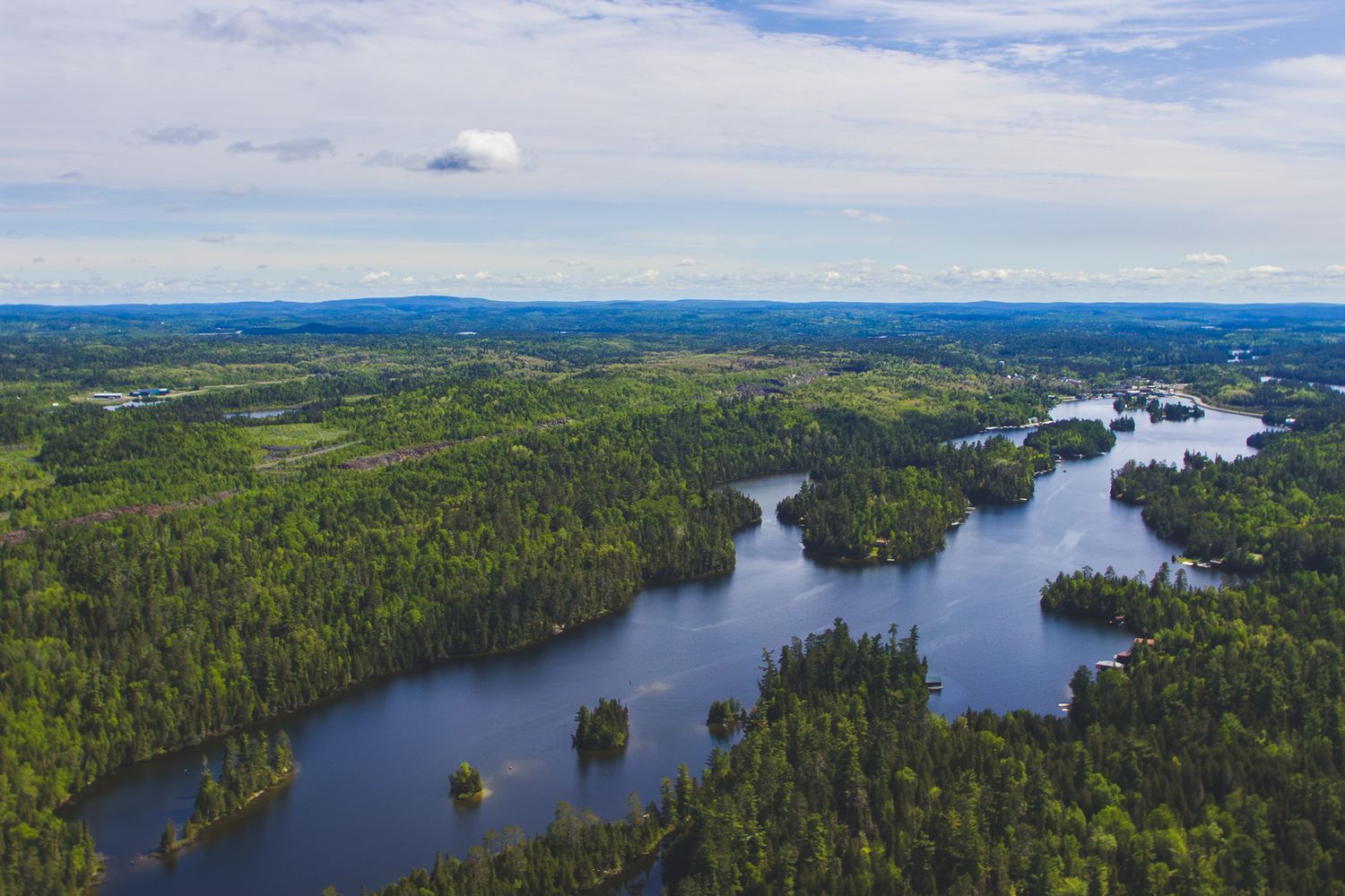 Aerial view of a serene lake system winding through dense forest landscape under cloudy sky in remote wilderness.