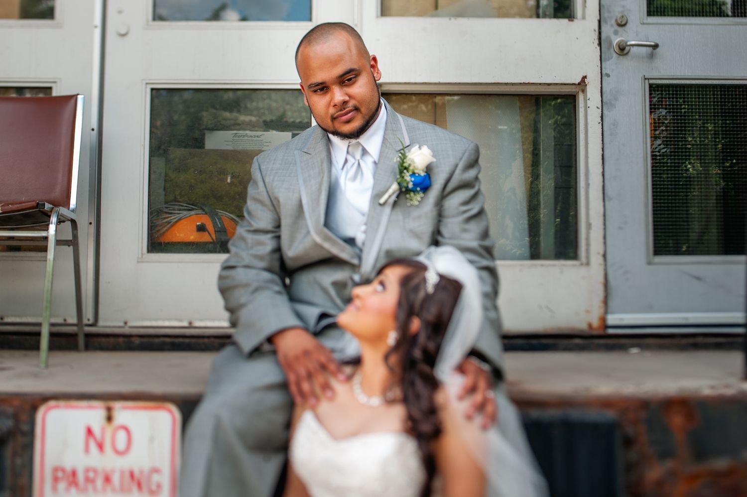A joyful wedding couple shares an intimate moment while sitting by a no parking sign in formal attire.