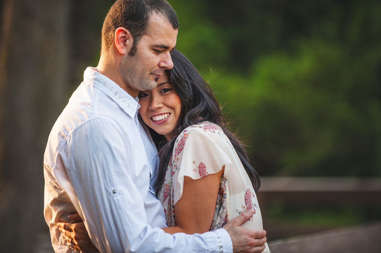 A couple embraces intimately outdoors during golden hour with a blurred forest background.