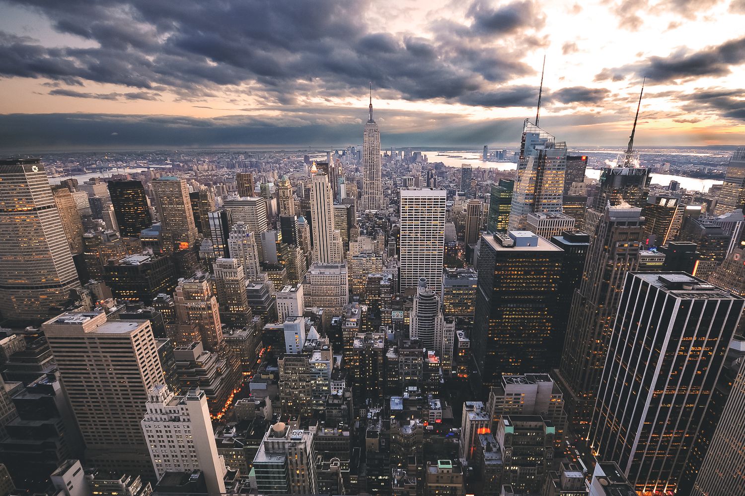 Dramatic aerial view of Manhattan's skyline at sunset with moody clouds over skyscrapers.