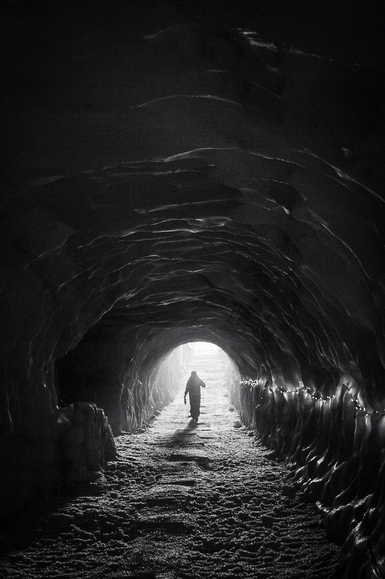 Silhouetted figure walking towards bright light at the end of a dark tunnel.