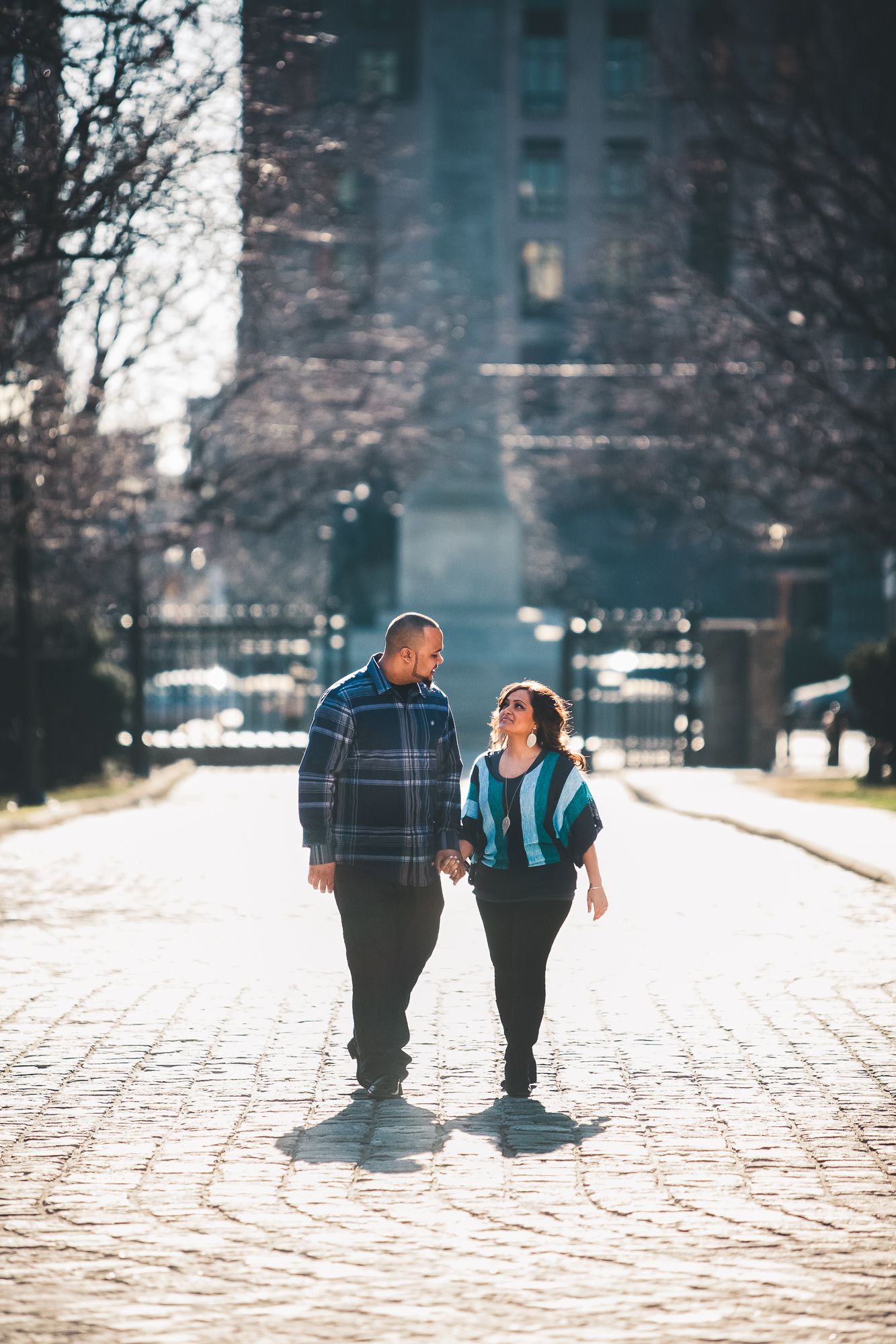 A couple walks together holding hands on a cobblestone path outside during a sunny winter afternoon.