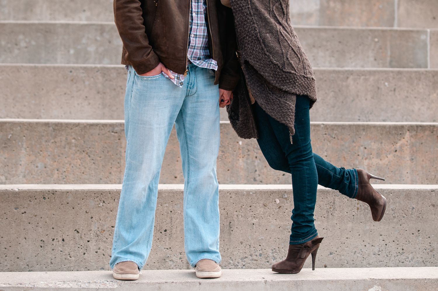 Two pairs of legs in contrasting styles with light blue jeans and dark skinny jeans on concrete steps.