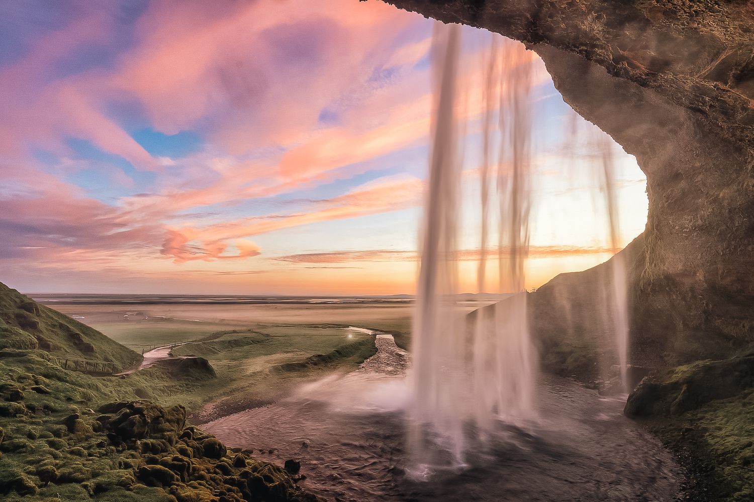 Stunning sunset view behind Seljalandsfoss waterfall in Iceland through a cave opening.