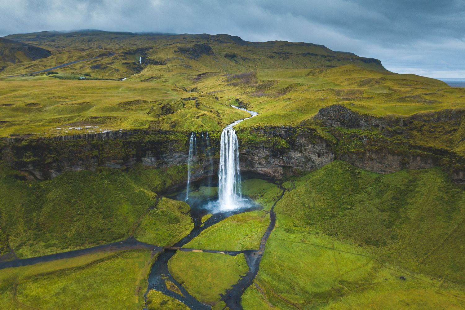 Dramatic Seljalandsfoss waterfall cascades down green cliffs in Iceland with winding rivers below and rolling hills.