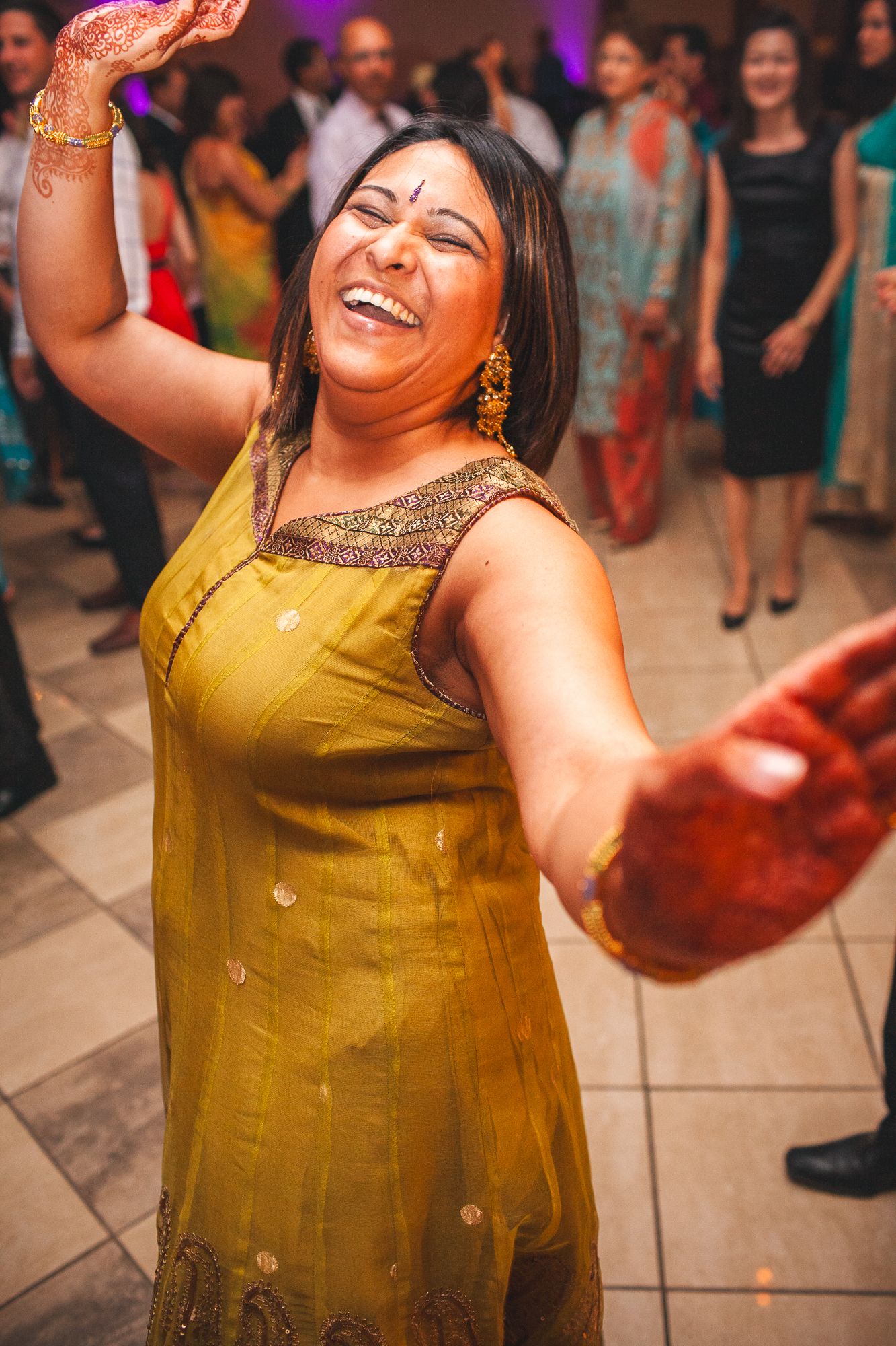 Dancer in yellow traditional Indian dress dances joyfully at a cultural celebration with festive crowd in background.