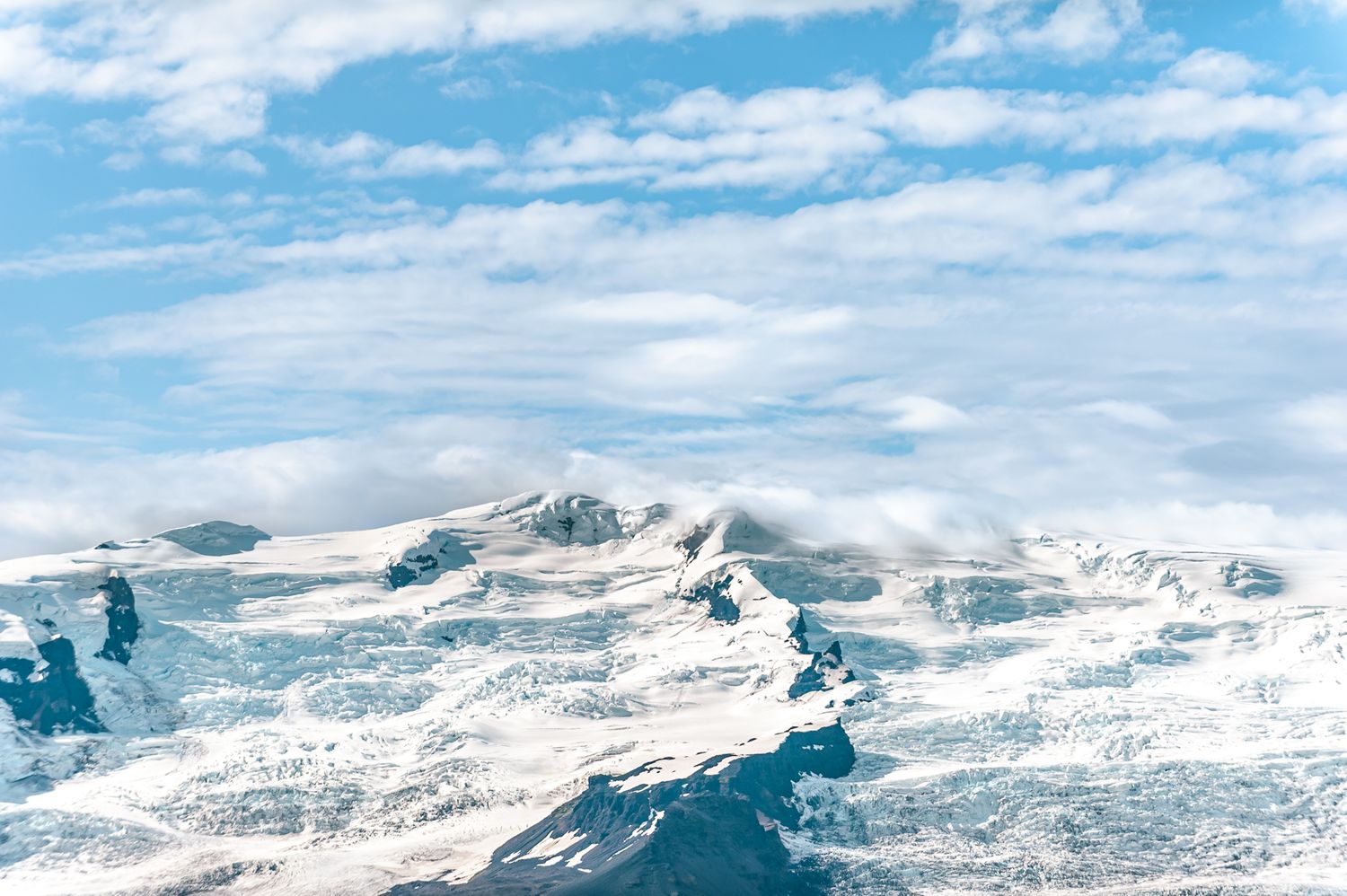 Snow-covered mountain peaks rise into a bright blue sky streaked with wispy white clouds on a clear winter day.