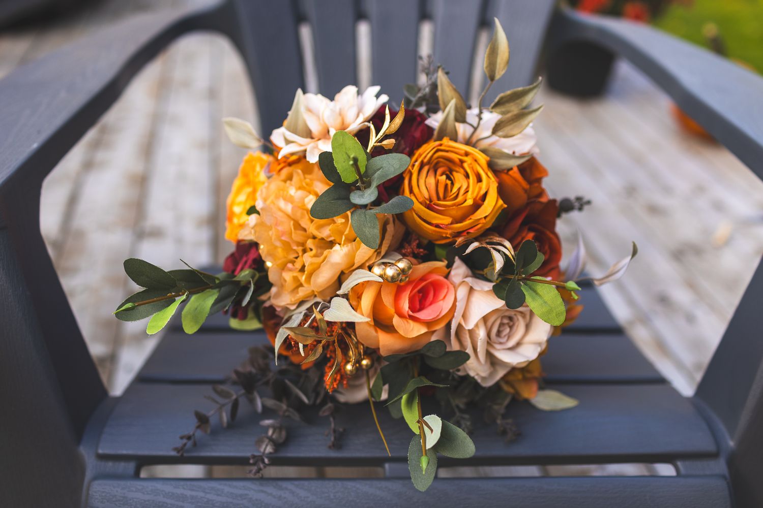 A beautiful autumn wedding bouquet with orange roses and mixed flowers sitting on a gray chair.