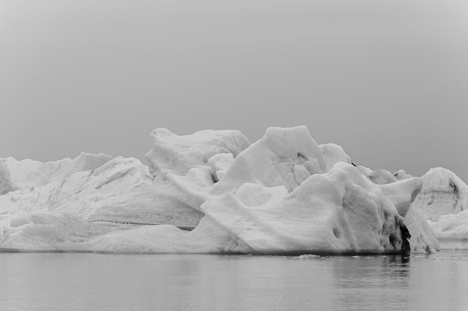 Black and white photograph of a dramatic glacial ice formation reflected in calm arctic waters.