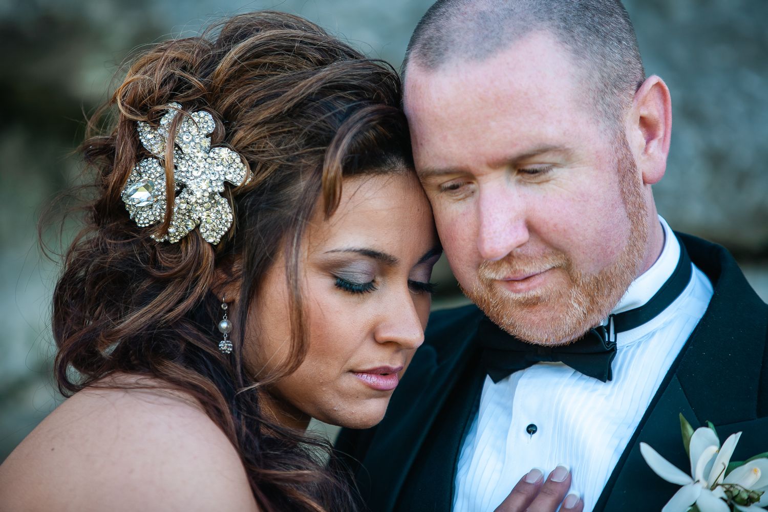 A bride wearing a sparkly hair accessory and groom in a black tuxedo share an intimate moment during their wedding day.