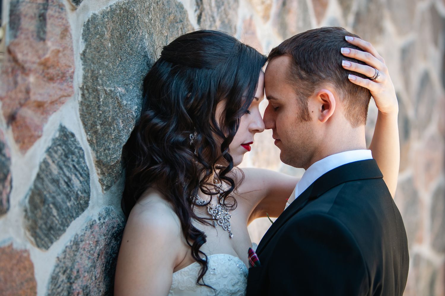 A tender romantic moment between newlyweds against a rustic stone wall.