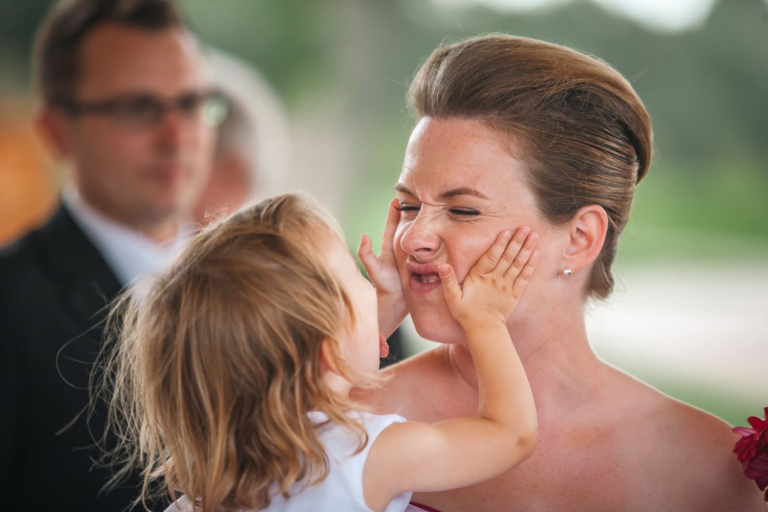 A tender moment shared between a bride in a red gown and a young child during a wedding celebration.