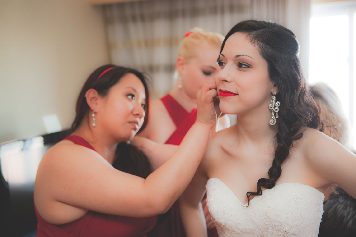 Final wedding preparations in progress as bridesmaids help with makeup adjustments in a softly lit room.