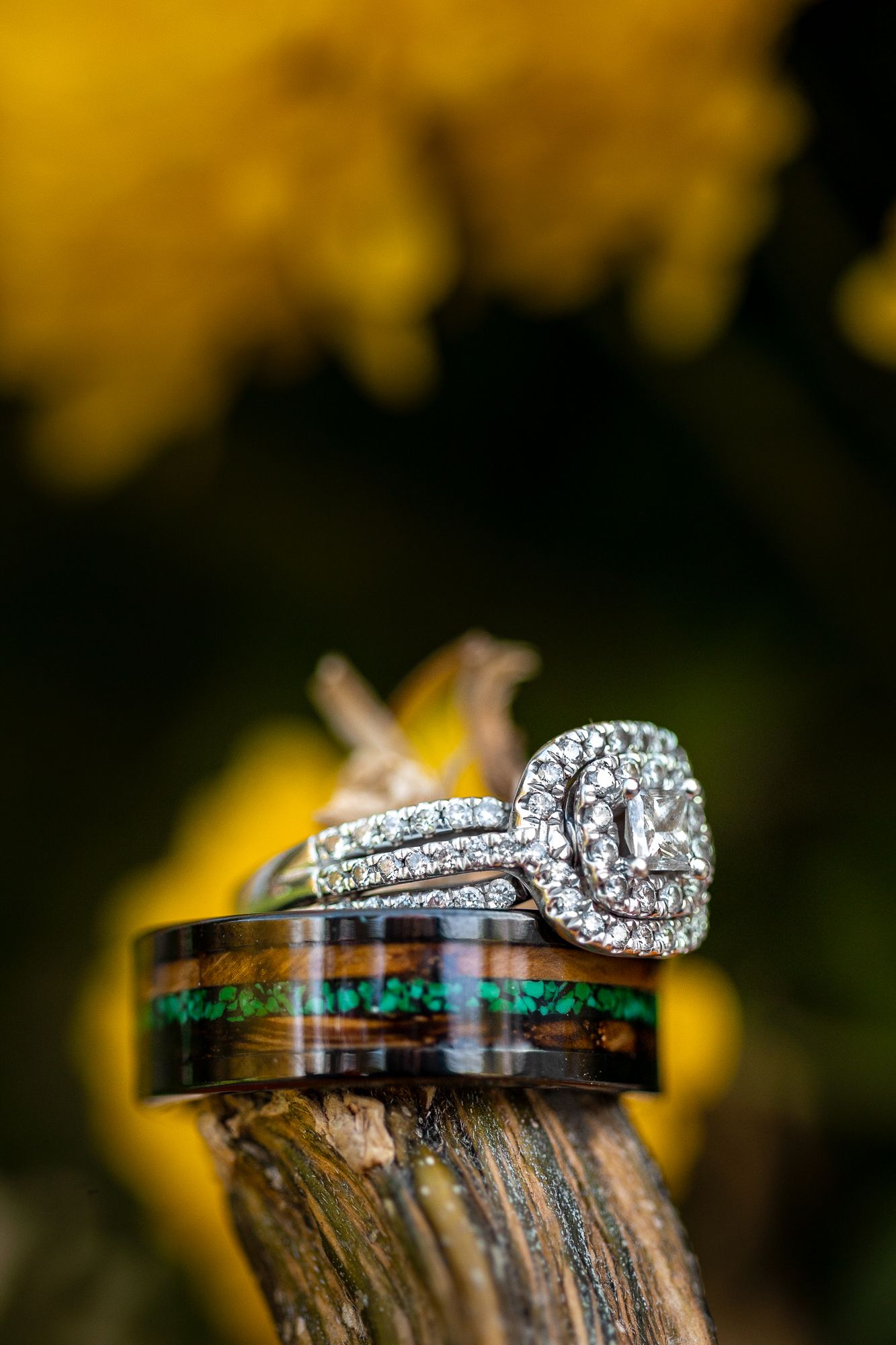 Diamond engagement ring and colorfully inlaid wedding band displayed on a wooden surface with golden bokeh background.