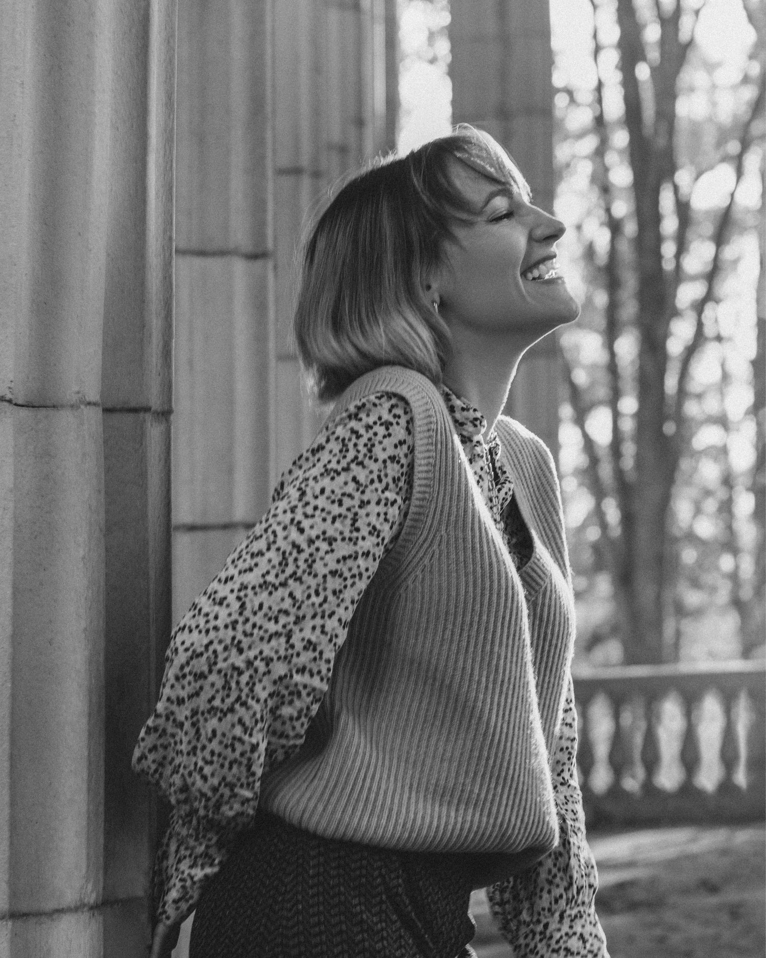 Candid portrait of a woman leaning against a column, laughing joyfully during a cinematic photoshoot