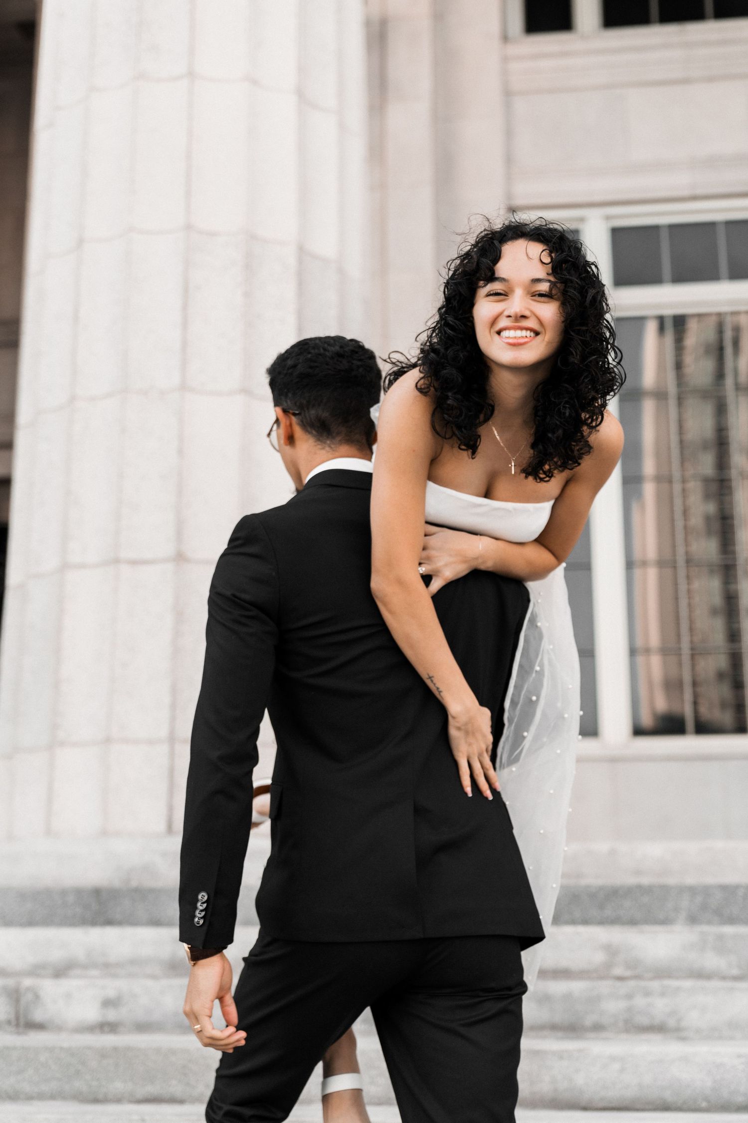 Candid Miami engagement (elopement/mini wedding) photoshoot – groom carrying bride toward courthouse as she laughs