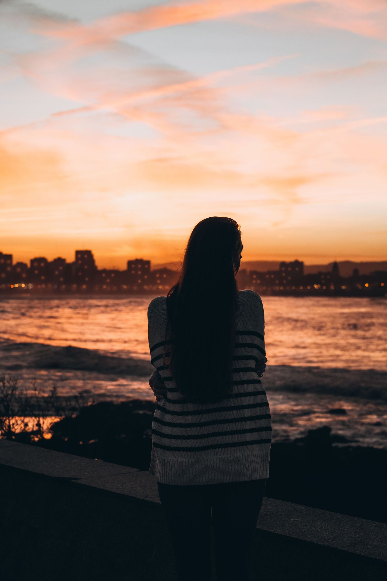 Portrait of a woman standing, gazing at the sunset, her silhouette outlined against the golden sky during a photoshoot