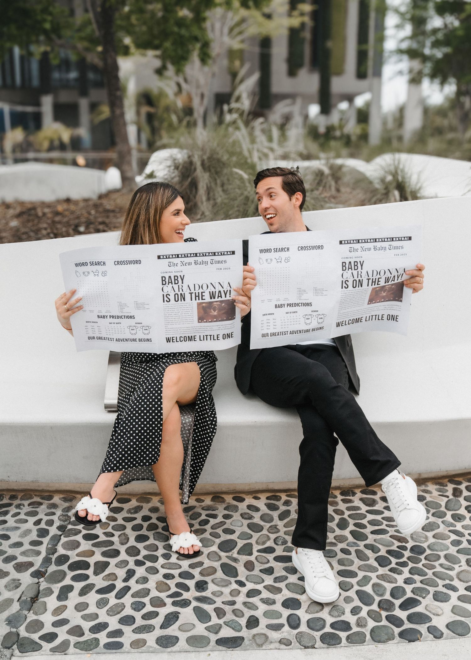 Expecting couple on a bench in Miami – holding pregnancy announcement newspapers with joyful, surprised expressions