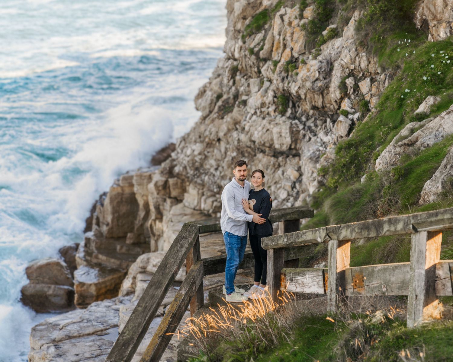 Couple embracing on the stairs by the cliffs and ocean during a cinematic lifestyle photoshoot