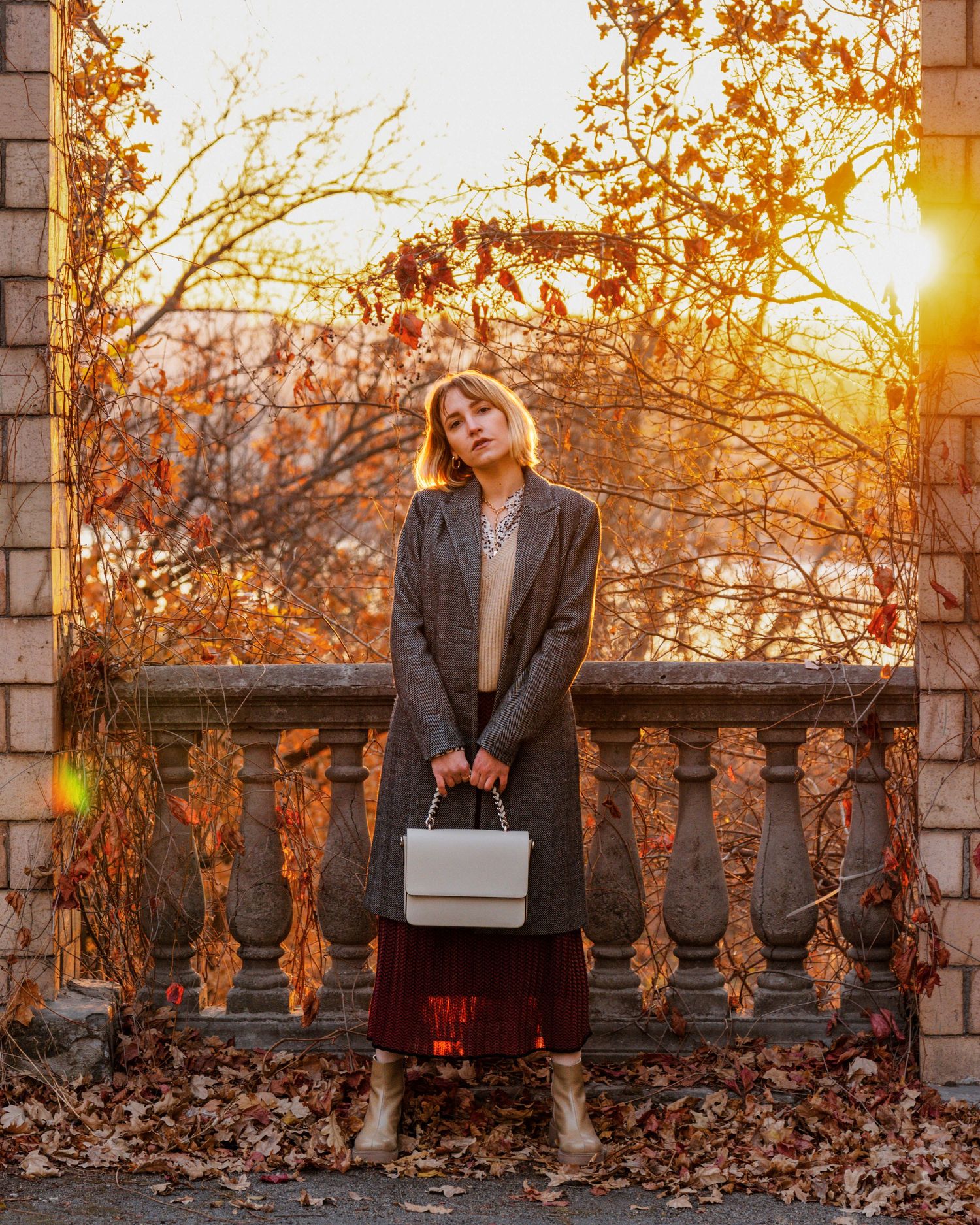 Editorial-style fashion portrait of a woman standing with the sunset behind her, captured in a cinematic moment