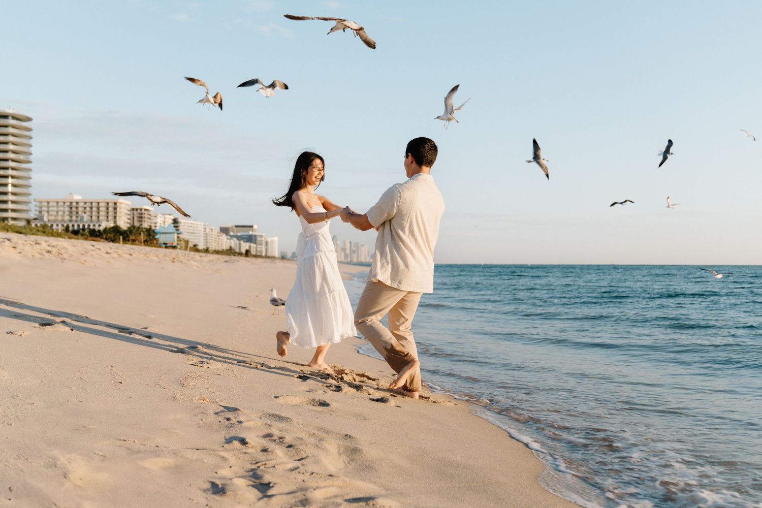 Candid Miami beach photoshoot – couple spinning joyfully, surrounded by seagulls