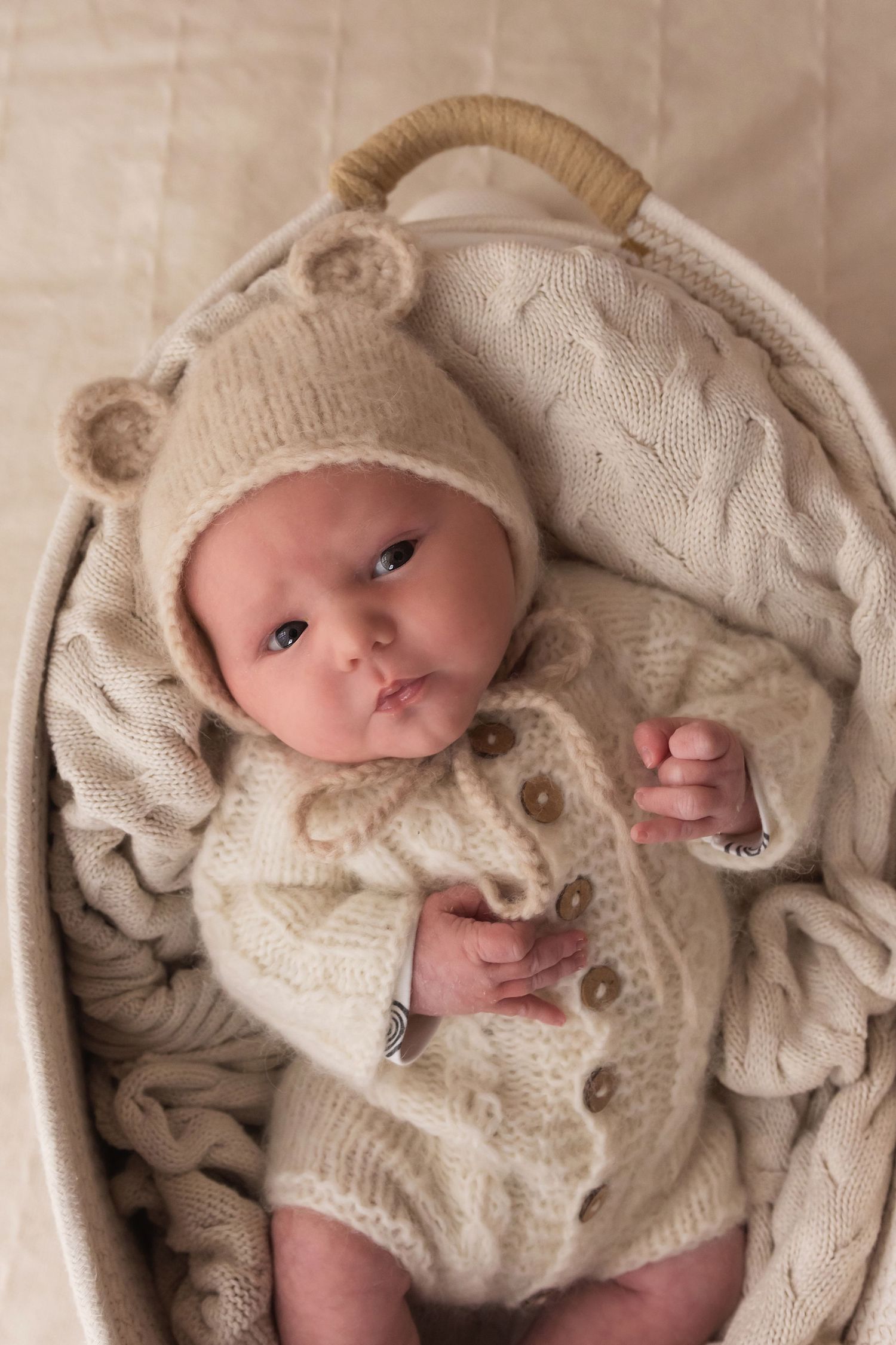 Newborn baby in cream knit bear outfit resting peacefully in a wicker basket.